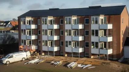 Byggematerialer foran lejlighedskompleks med solen i baggrunden