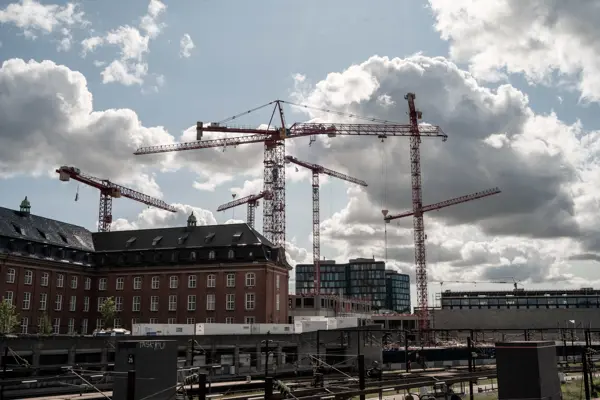 Høje kraner skyder op over tagene med togspor i forgrunden i København.