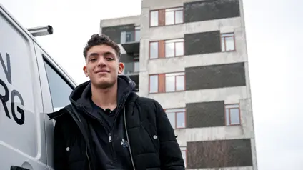 Ung fyr sår lænet op af bil og kigger smilende ind i kameraet