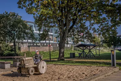 Barn sidder på en lege-traktor lavet af træ på en legeplads i boligafdelingen Skovparken