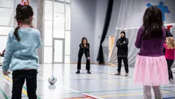 Børn i 6-års-alderen står og kigger på deres unge, kvindelige trænere i en gymnastiksal