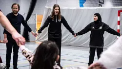 Kvindelige træner holder i hånden med to andre voksne, der danner en cirkel inde i en gymnastiksal