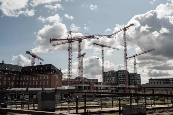 Høje kraner skyder op over tagene med togspor i forgrunden i København.